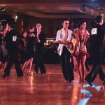 Casal executa uma coreografia de dança de salão em um palco iluminado.