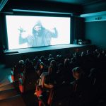Público acompanha a exibição de um filme em uma sala de cinema lotada.