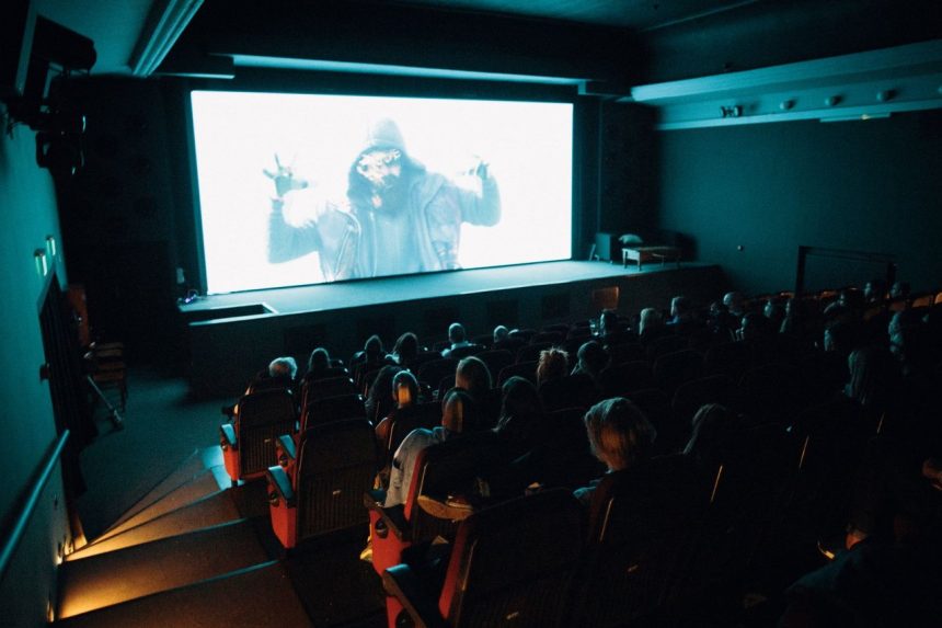 Público acompanha a exibição de um filme em uma sala de cinema lotada.