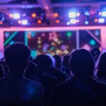 Pessoas vistas de costas acompanham um show enquanto luzes coloridas iluminam o palco.