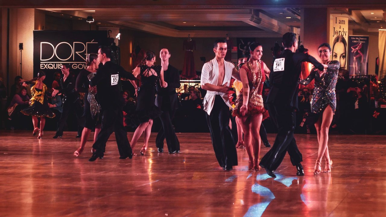 Casal executa uma coreografia de dança de salão em um palco iluminado.
