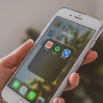 Mão segurando um smartphone com aplicativos de música exibidos na tela.