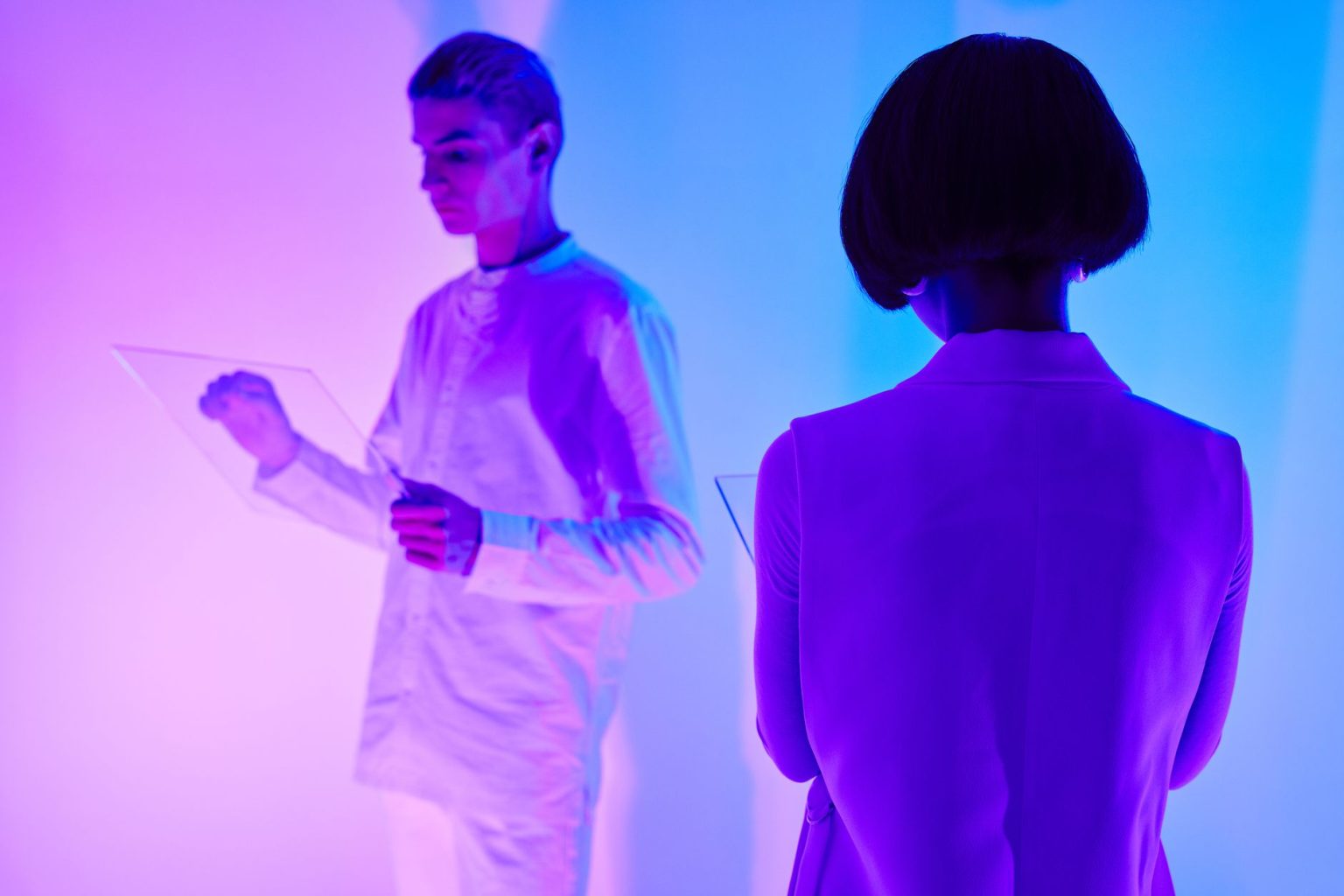 Duas pessoas interagem com interfaces digitais em um ambiente futurista iluminado por cores vibrantes.