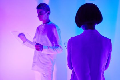 Duas pessoas interagem com interfaces digitais em um ambiente futurista iluminado por cores vibrantes.